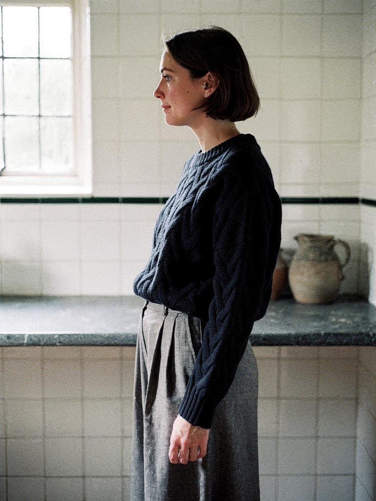 Cropped cable knit jumper in Ink Blue worn with grey wide trousers