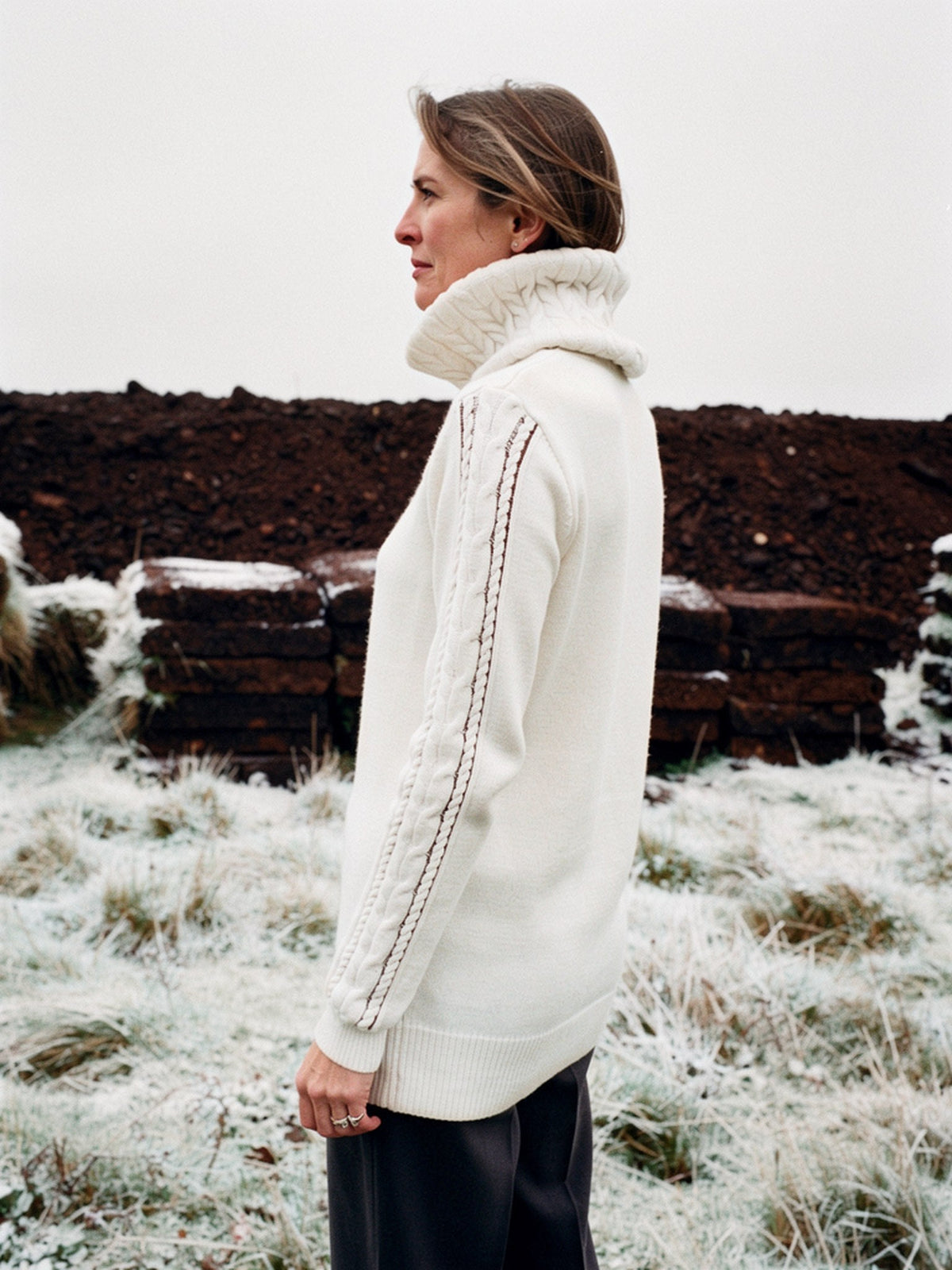 Womens cable knit roll neck jumper in Cream seen from behind on a winter moor