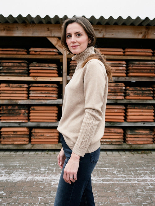 Womens cable knit roll neck jumper in Fawn worn with jeans at an English tile works
