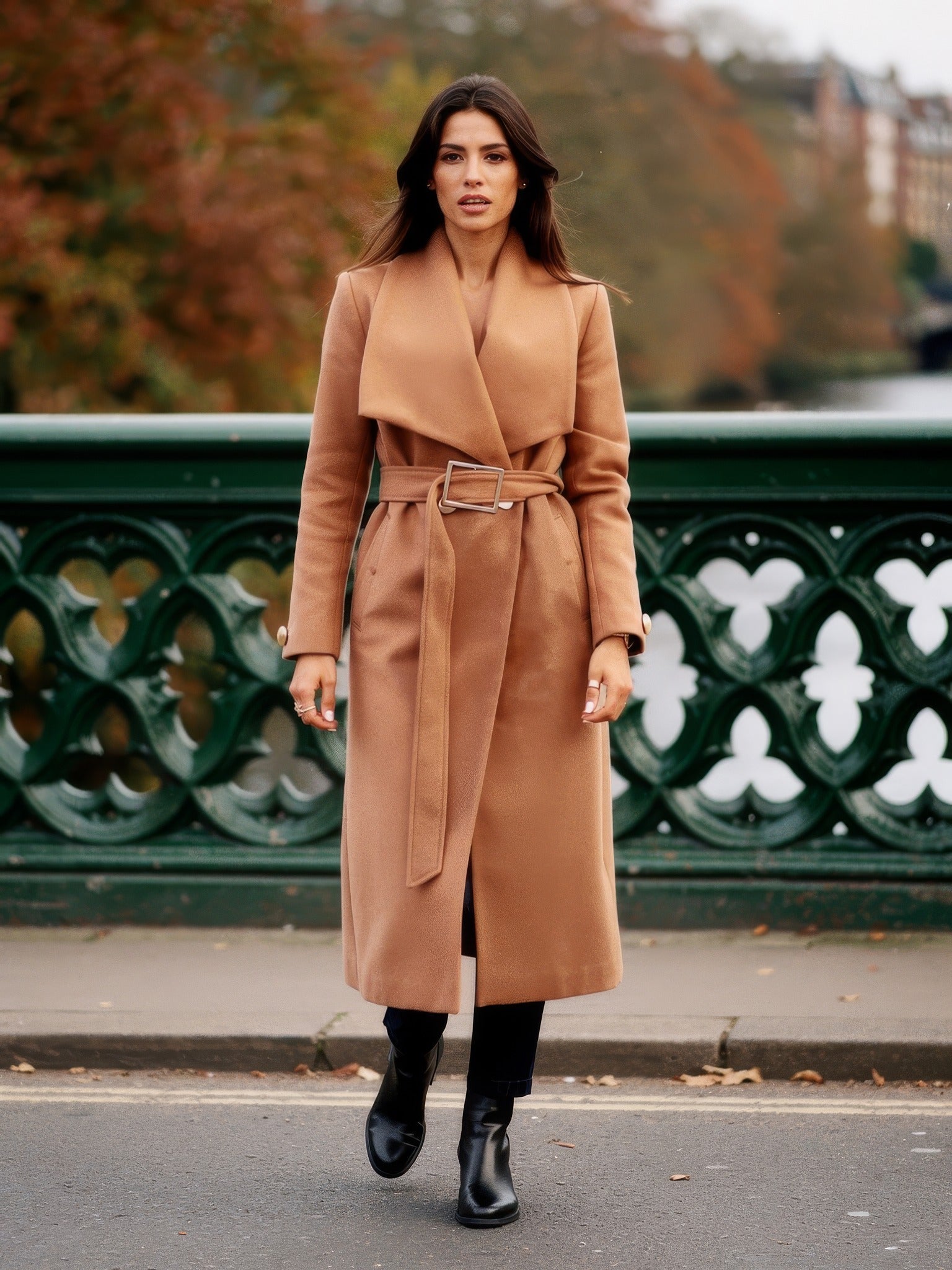 Woman wearing a camel belted longline wrap coat on a cast iron footbridge in autumn