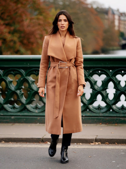 Woman wearing a camel belted longline wrap coat on a cast iron footbridge in autumn