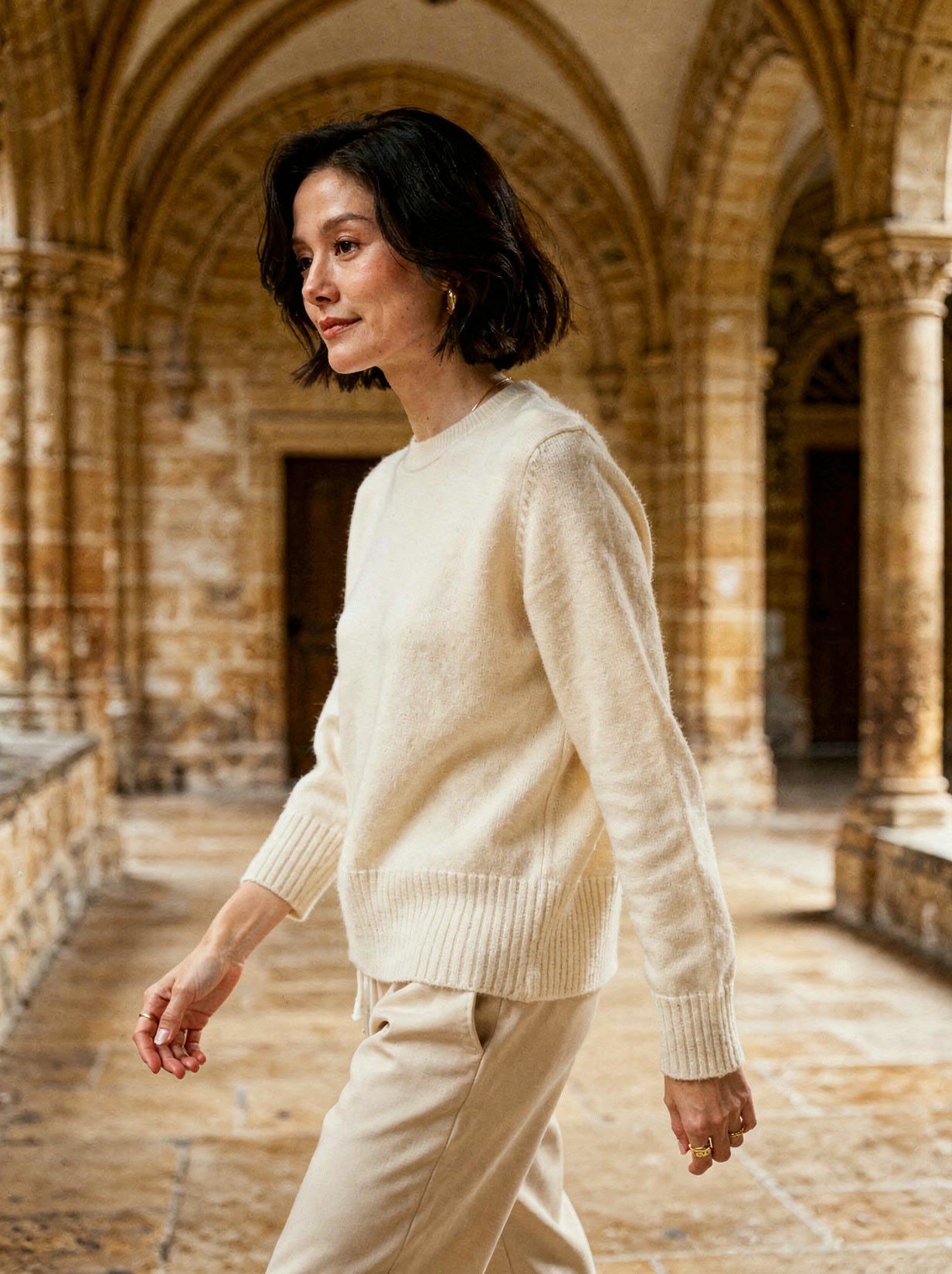 Winter white cashmere crew-neck jumper worn in a stone cathedral cloister