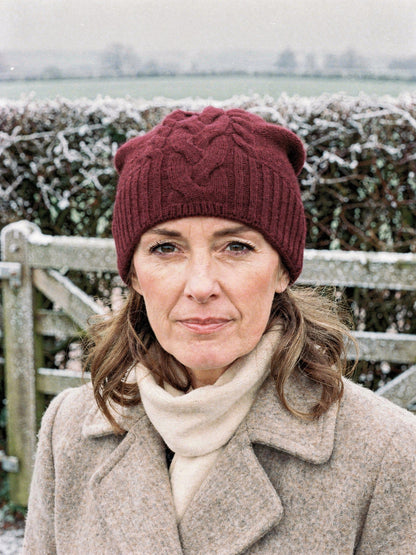 Woman wearing a burgundy cashmere hat with a plaited cable front at a frosted field gate