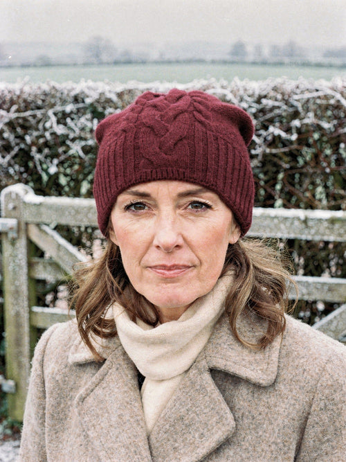 Woman wearing a burgundy cashmere hat with a plaited cable front at a frosted field gate