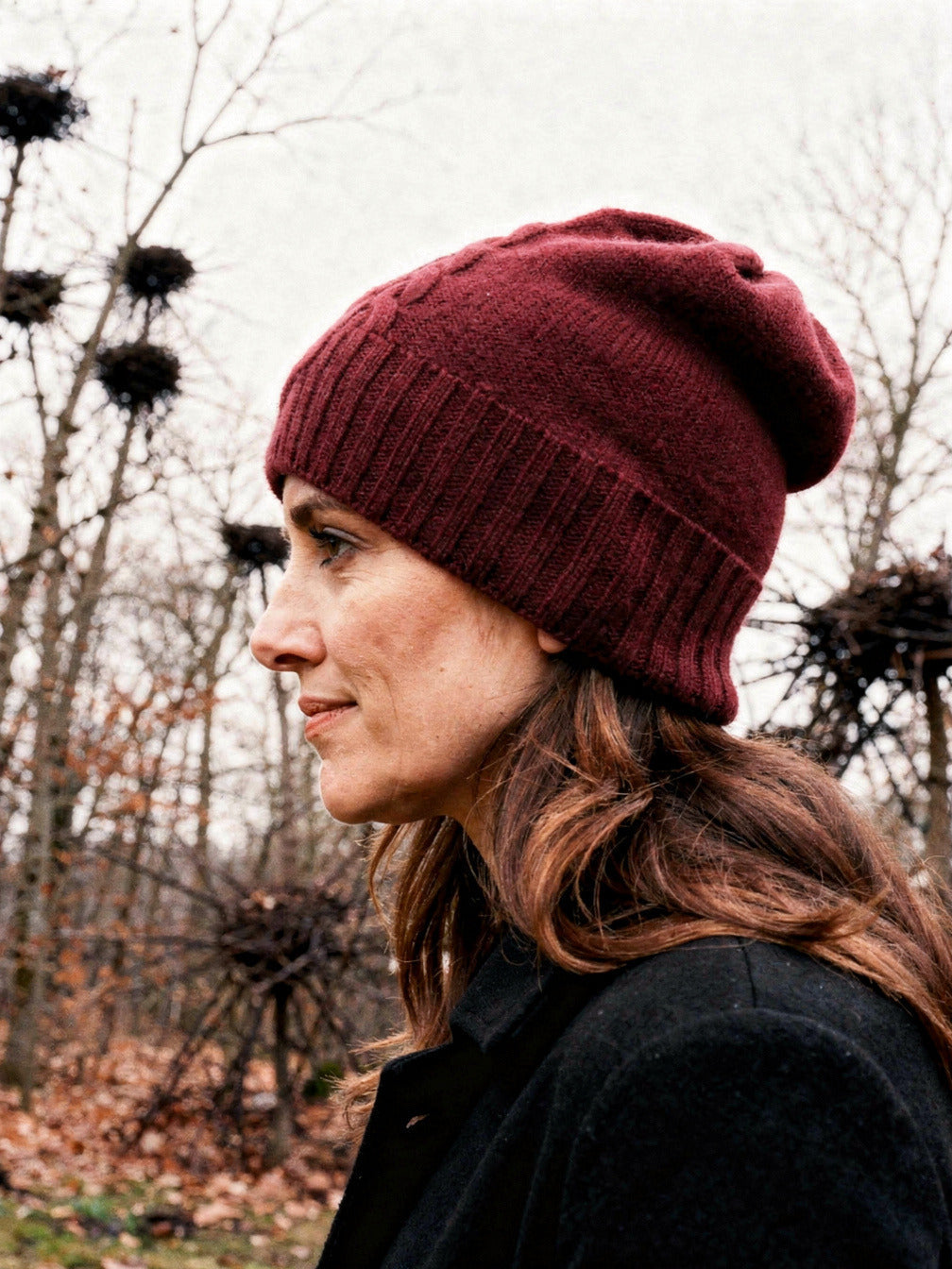 Side view of a burgundy cashmere hat worn slouched, showing the plain knitted side