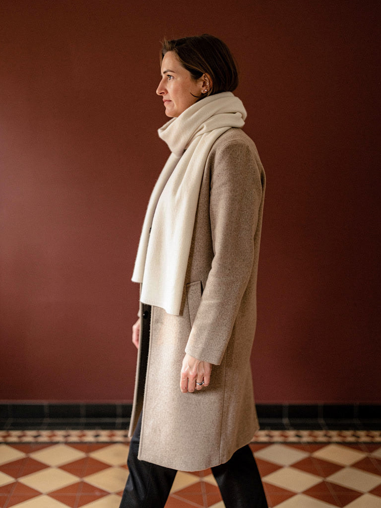 Parchment cashmere scarf worn open over an oatmeal coat in a Victorian tiled hall