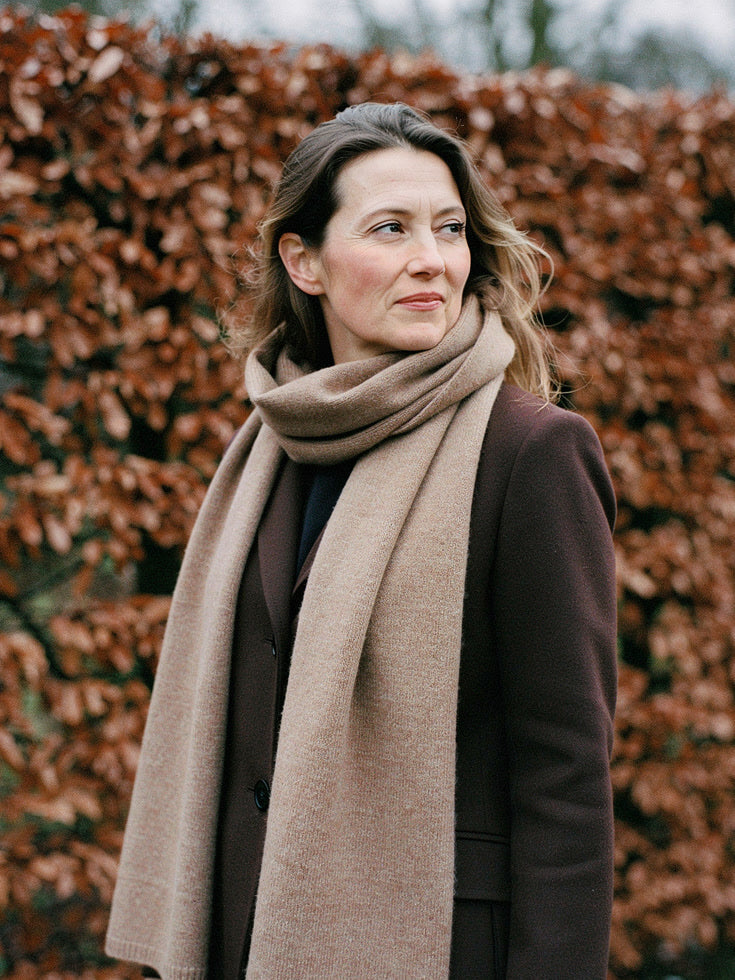 Woman wearing a Truffle cashmere scarf looped twice at the neck in front of a winter beech hedge
