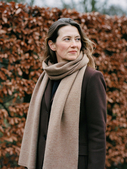 Woman wearing a Truffle cashmere scarf looped twice at the neck in front of a winter beech hedge