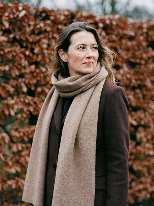 Woman wearing a Truffle cashmere scarf looped twice at the neck in front of a winter beech hedge