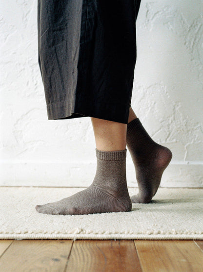 Cashmere socks in Mushroom worn on a cream wool rug over bare oak boards