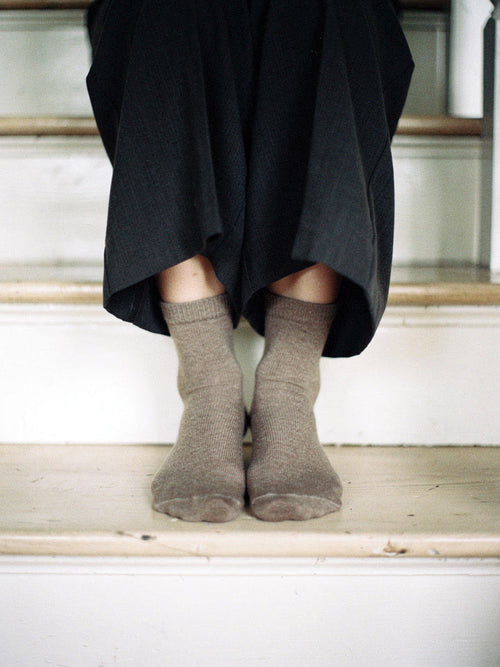 Cashmere socks in Mushroom worn on a white cottage staircase, fine ribbed mid-calf knit