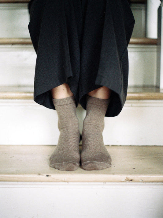Cashmere socks in Mushroom worn on a white cottage staircase, fine ribbed mid-calf knit