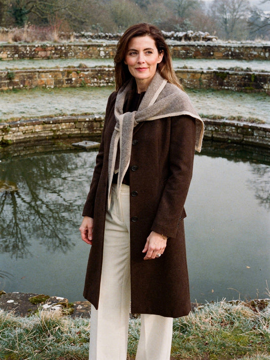 Cashmere triangle scarf in Clay worn open across the shoulders beside frosted terraced ponds