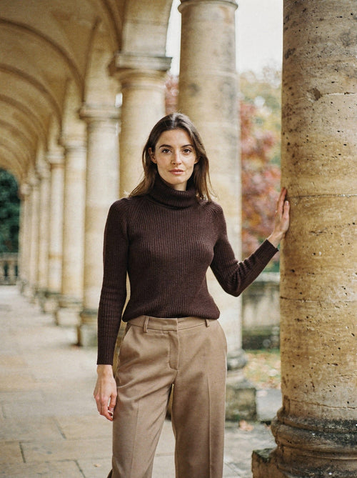 Woman wearing the espresso cashmere turtleneck jumper under a Georgian stone colonnade