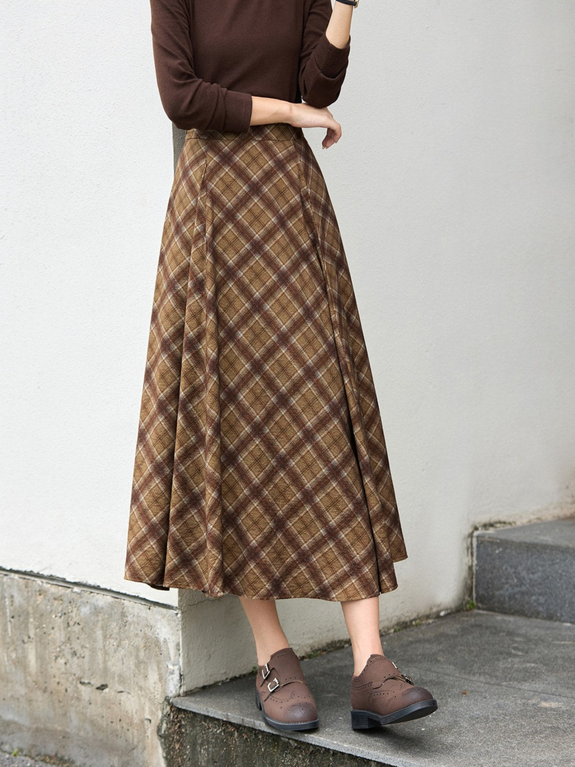 Checked pleated skirt worn with brown loafers, showing the midi length low on the calf
