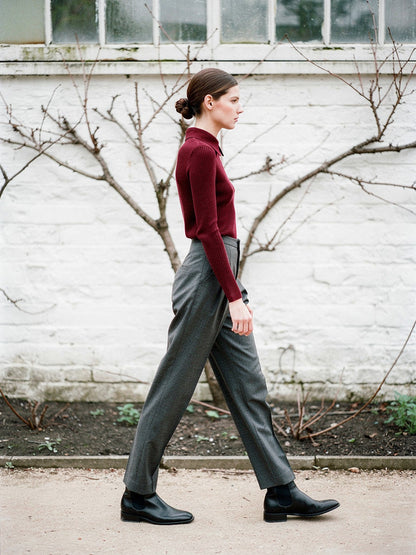 Bordeaux collared jumper worn with charcoal trousers, side view, showing the knitted point collar against a whitewashed garden wall