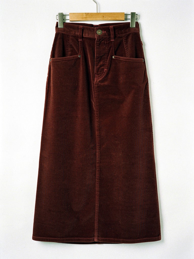 Corduroy skirt in Amarone burgundy on a wooden hanger, front view, showing the angled rivet pockets, the antique brass button and the level hem