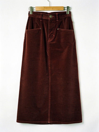 Corduroy skirt in Amarone burgundy on a wooden hanger, front view, showing the angled rivet pockets, the antique brass button and the level hem