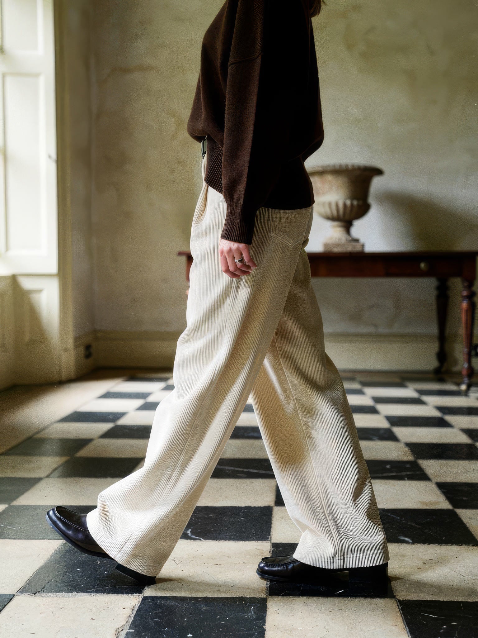 Corduroy wide-leg trousers in Parchment worn walking across a chequerboard stone floor