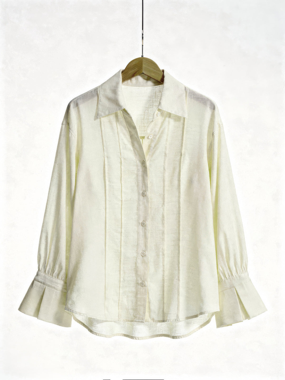 Cream blouse on a wooden hanger showing the pintuck front, point collar and fluted cuffs