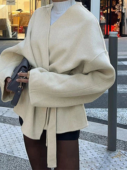 Cream collarless wrap jacket seen from behind, showing the wide dolman sleeves and the hanging belt