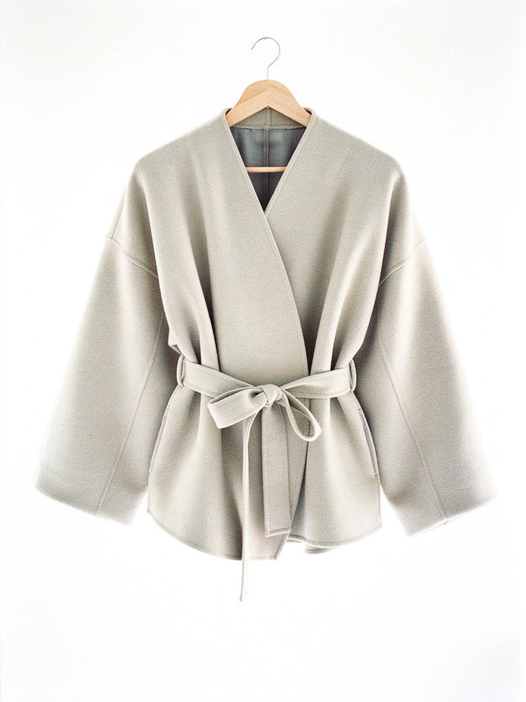 Cream collarless wrap jacket in Eggshell shown on a hanger with the tie belt knotted