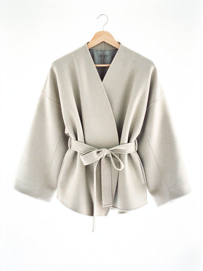 Cream collarless wrap jacket in Eggshell shown on a hanger with the tie belt knotted