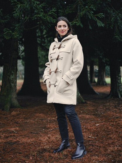 Cream hooded coat worn fastened in a grove of ancient yews, toggle front, hands in the patch pockets