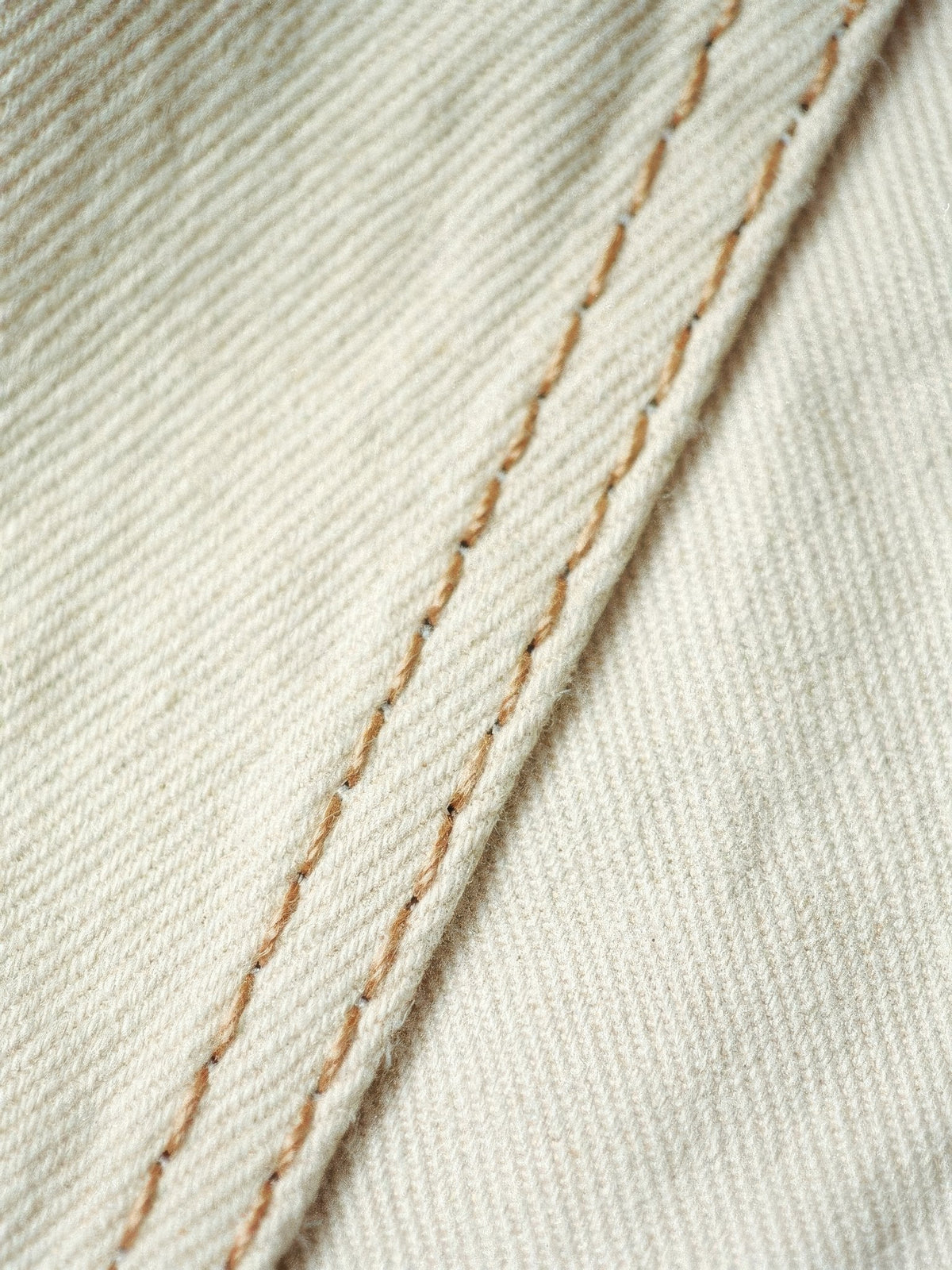 Close-up of the pale cream cotton denim twill and camel contrast topstitching of the cream jeans