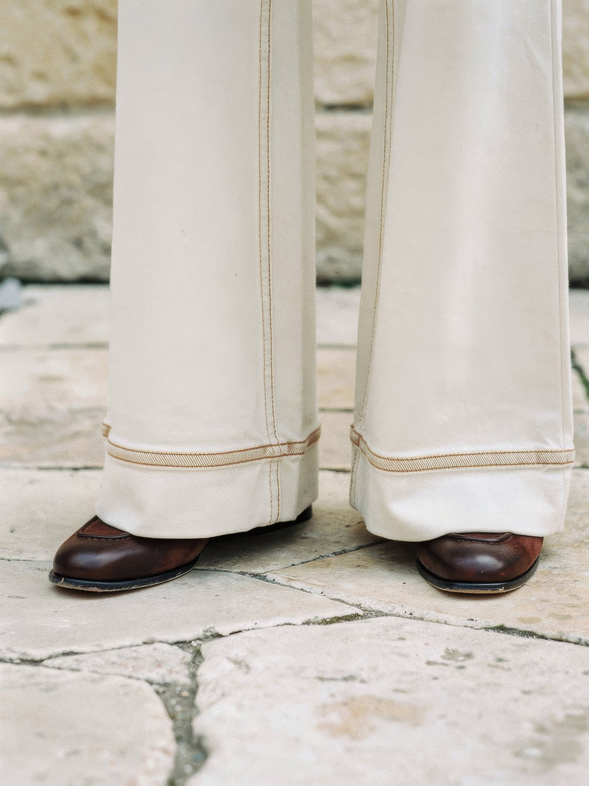 Wide hem of the cream jeans with two lines of camel stitching, falling over brown leather shoes