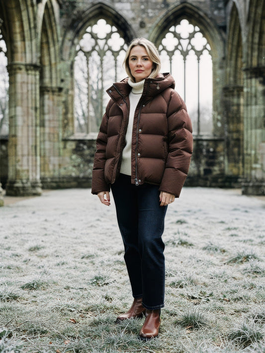 Womens cropped puffer jacket in Truffle Brown worn open over a cream roll neck in English abbey ruins