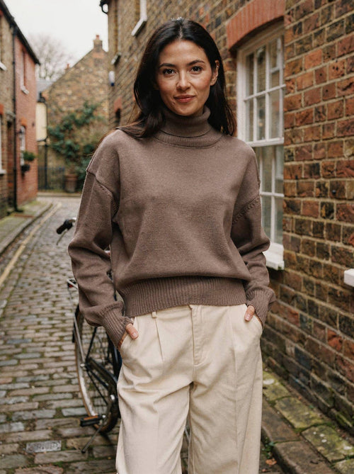 Woman wearing the taupe cropped turtleneck jumper with cream trousers in a cobbled mews street
