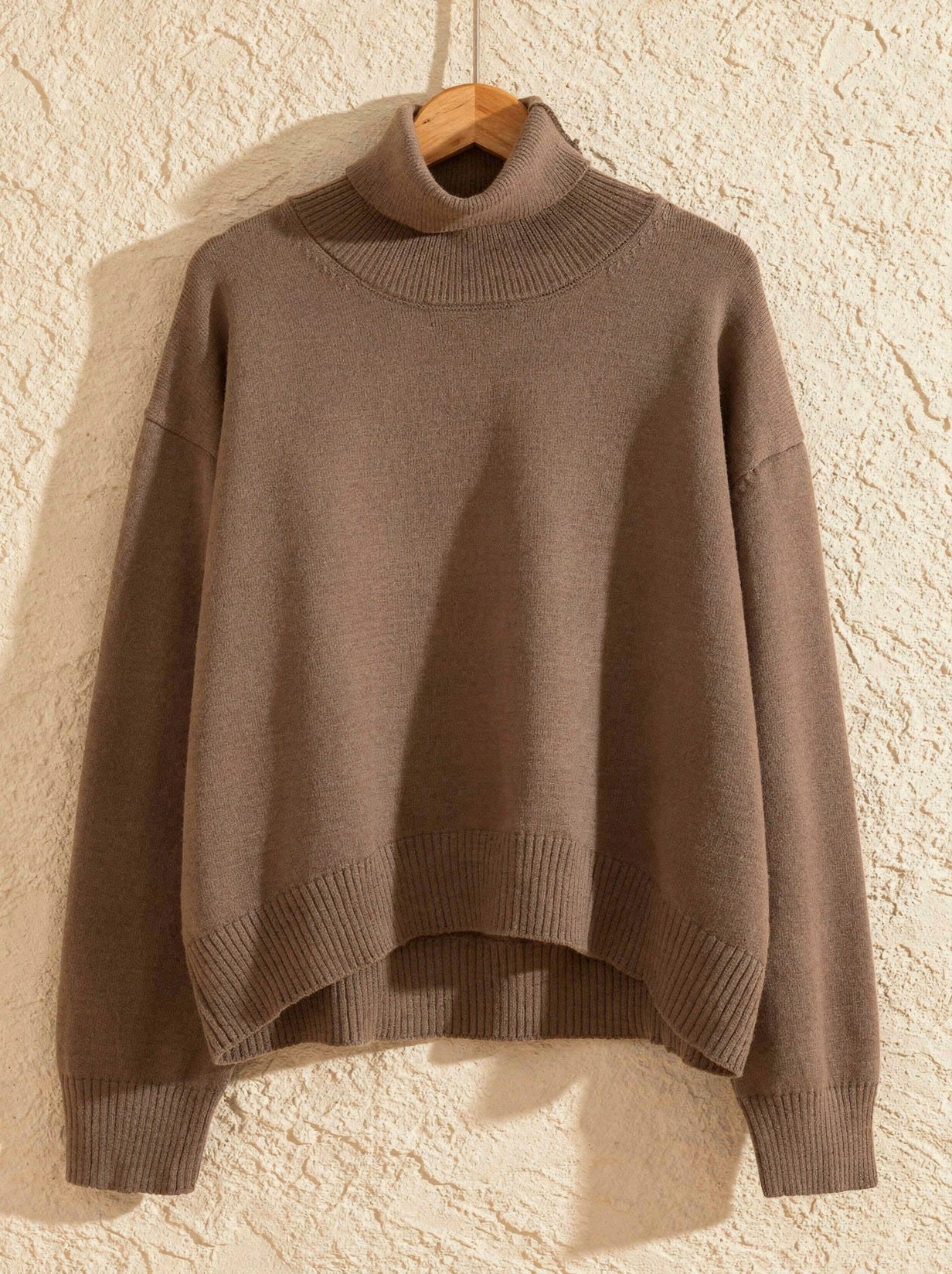 Taupe cropped turtleneck jumper on a wooden hanger showing the boxy shape and ribbed hem band