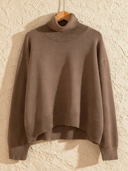 Taupe cropped turtleneck jumper on a wooden hanger showing the boxy shape and ribbed hem band