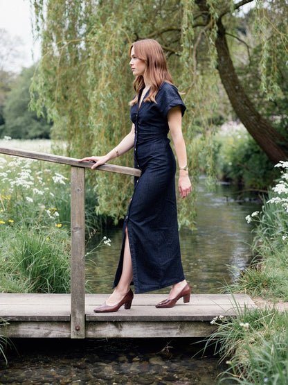 Denim maxi dress seen in profile on a footbridge over a chalk stream