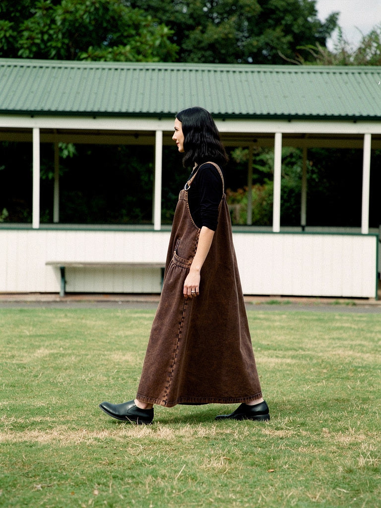 Side view of the Rust Wash denim pinafore dress, full A-line skirt to the ankle