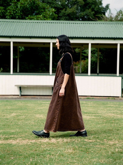 Side view of the Rust Wash denim pinafore dress, full A-line skirt to the ankle