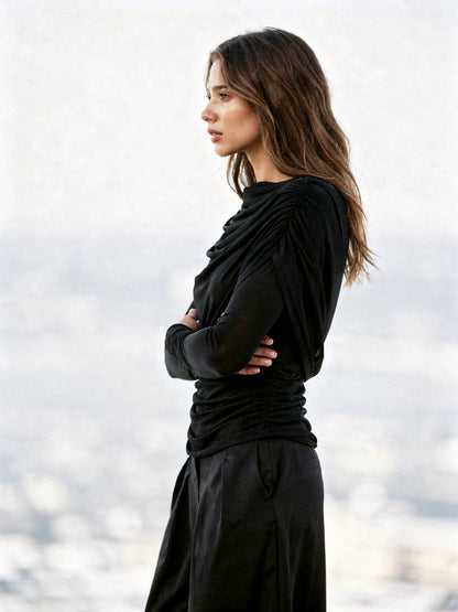 Side view of the black draped top, showing the gathered side seam and the long fitted sleeve