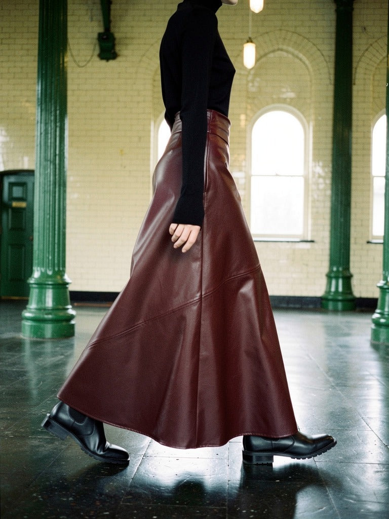 Faux leather maxi skirt in garnet seen from the side, the A-line hem swinging as she walks