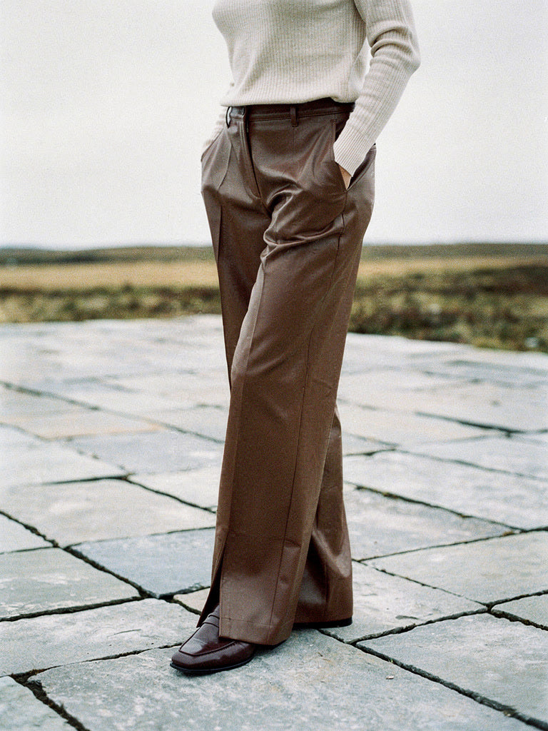 Womens chestnut faux leather trousers worn full length on a limestone pavement