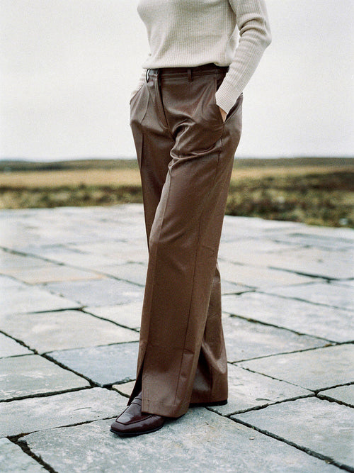 Womens chestnut faux leather trousers worn full length on a limestone pavement