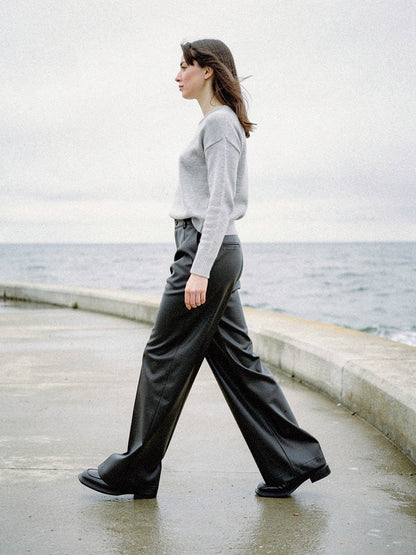 Jet black faux leather trousers worn walking along a concrete sea wall