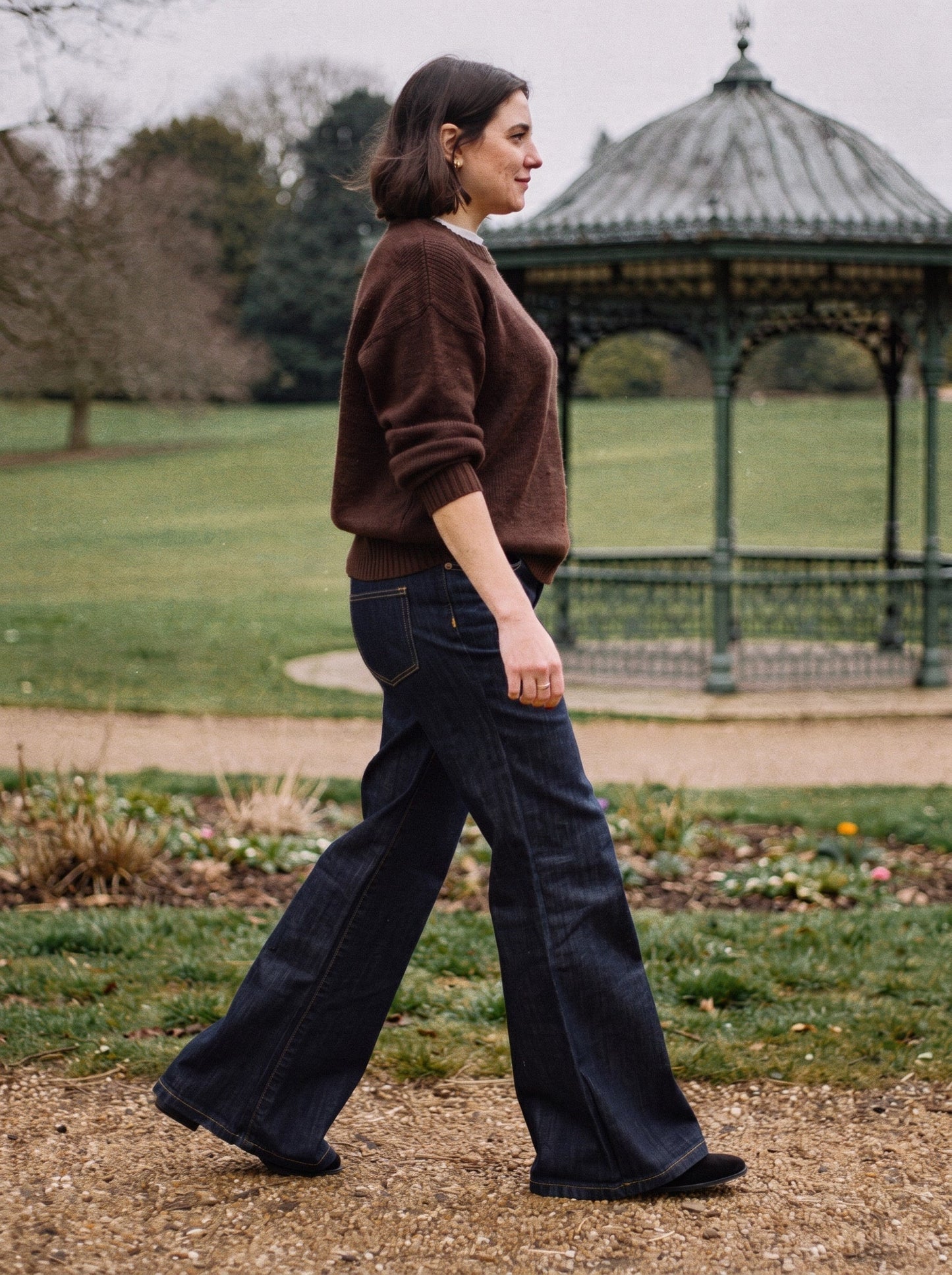 Side profile of dark indigo flared jeans in motion with a chocolate brown jumper in a park
