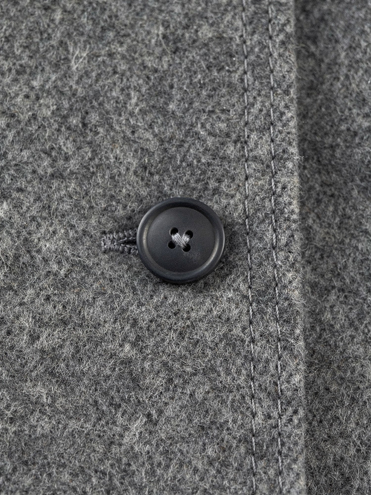 Close up of the brushed double faced wool and the flat four hole button of the grey wool coat