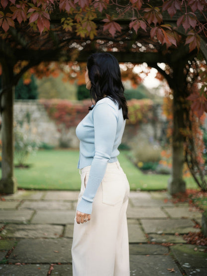 Woman wearing a powder blue cropped ribbed cardigan under a garden pergola