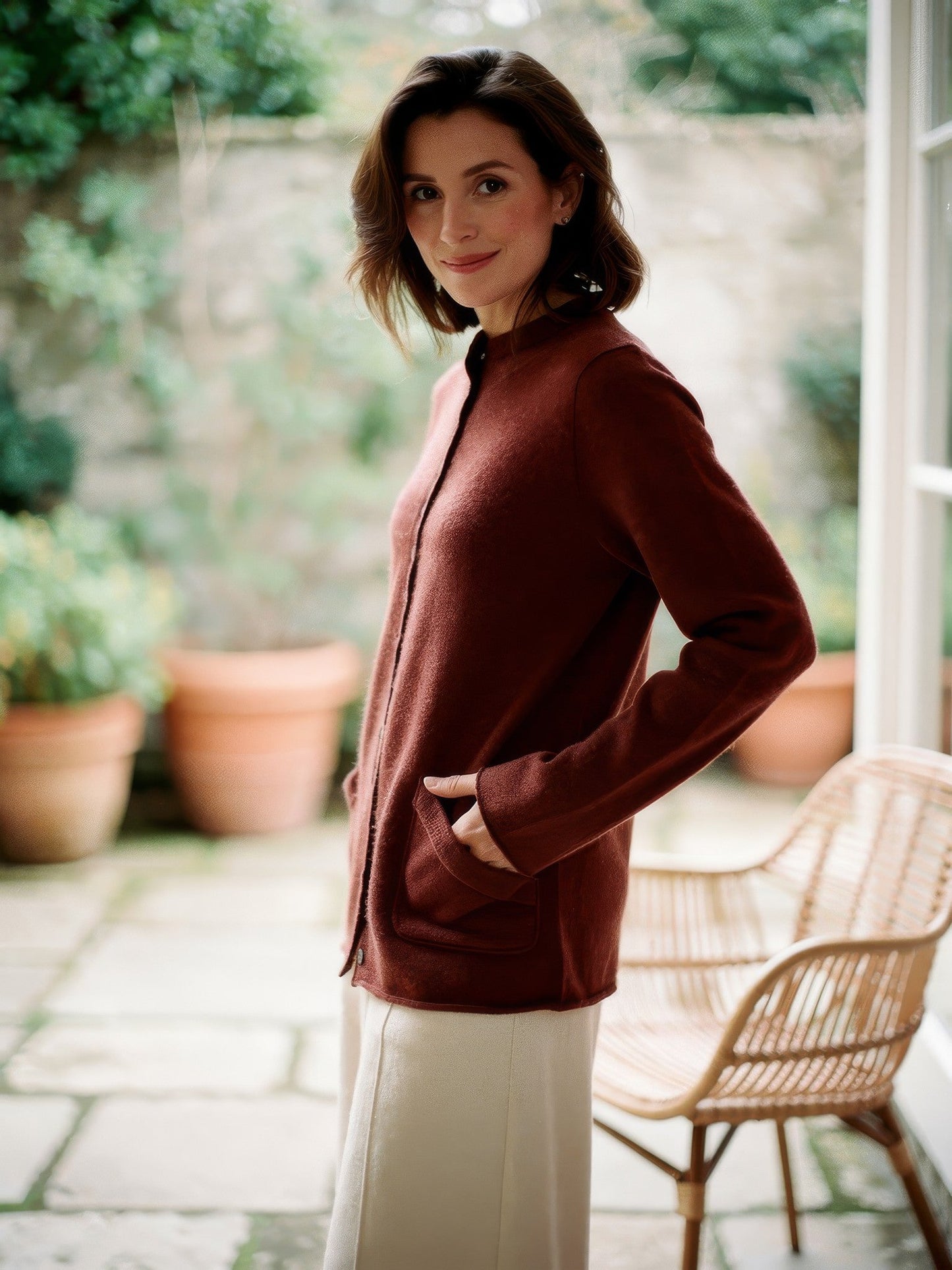 Rosewood mock-neck wool cardigan worn in a garden room