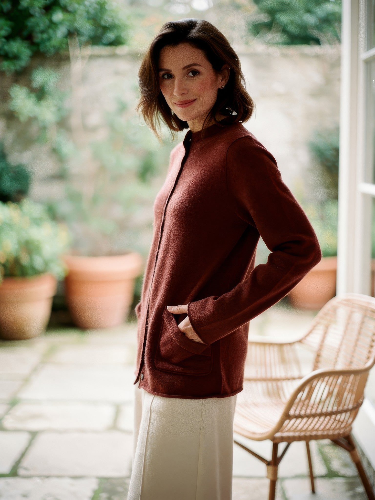Rosewood mock-neck wool cardigan worn in a garden room