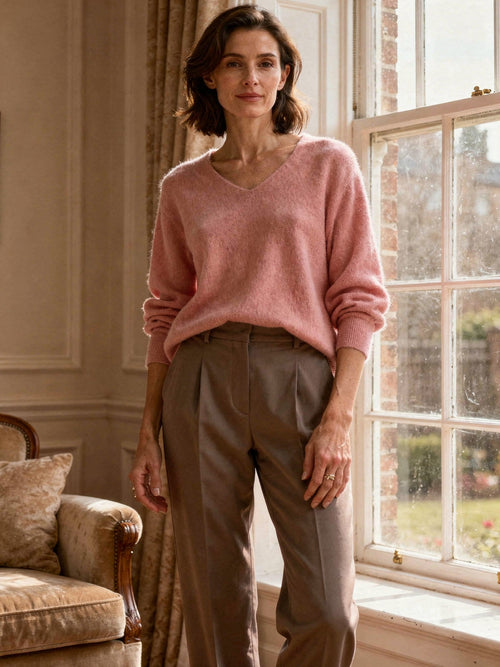 Woman wearing a Harlbury blush pink brushed V-neck jumper by a Georgian window