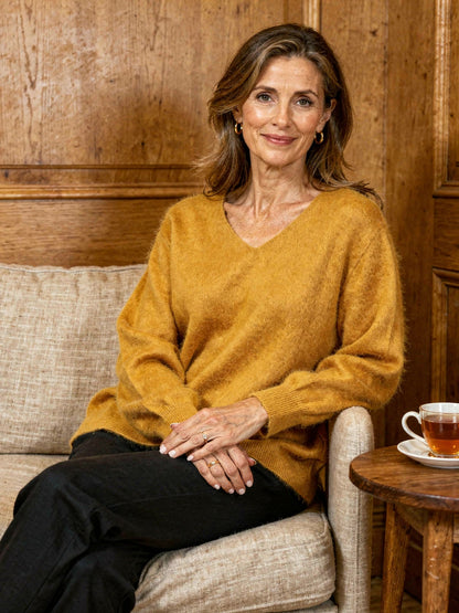 Woman wearing a Harlbury ginger brushed V-neck jumper on a linen sofa