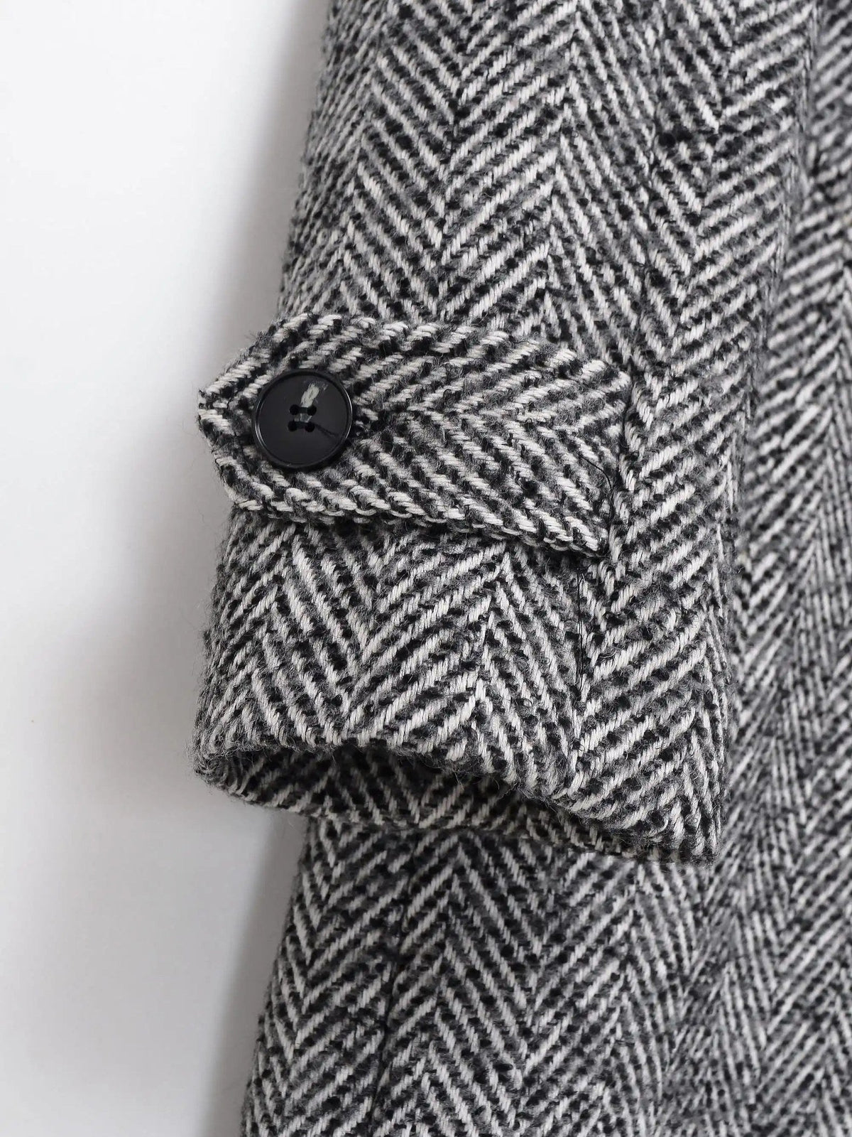 Buttoned tab on the sleeve cuff of the grey herringbone midi coat